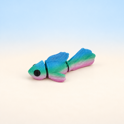 Micro Betta Fish 3D-printed miniature featuring a turquoise body and flowing multicolored fins, on a light surface with a pale blue background.
