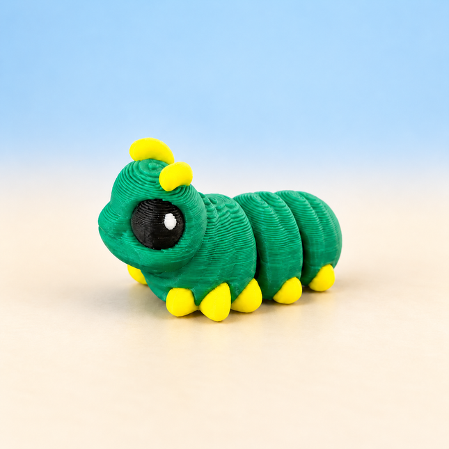 Micro Caterpillar 3D-printed miniature with a green segmented body, yellow feet, and yellow antennae, on a light surface against a pale blue background.