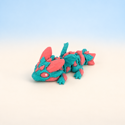 Micro Dragon 3D-printed miniature featuring a turquoise and pink body, small horns, and detailed wings, on a light surface with a pale blue background.