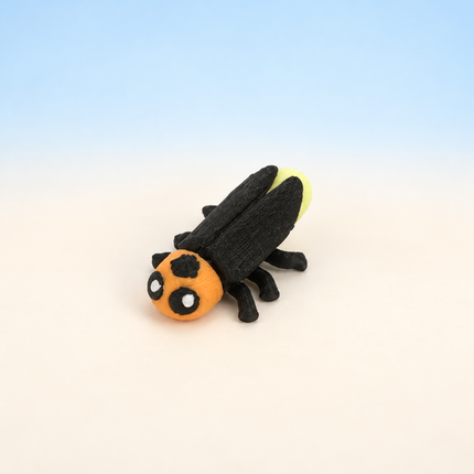 Micro Firefly 3D-printed miniature featuring a dark body, orange face, and long wings, on a light surface with a pale blue background.