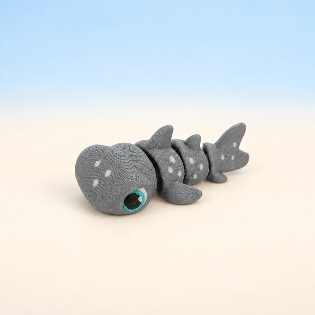 Micro Hammerhead Shark 3D-printed miniature featuring a gray body, wide hammer-shaped head, and spotted details, on a light surface with a pale blue background.