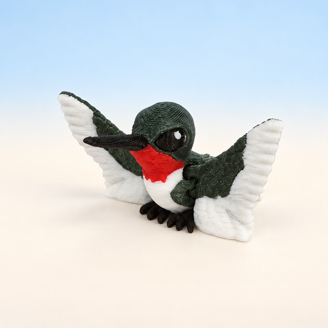 Micro Hummingbird 3D-printed miniature featuring a green body, red throat, long beak, and spread wings, on a light surface with a pale blue background.