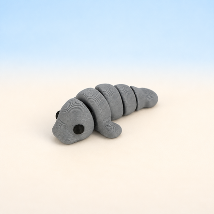 Micro Manatee 3D-printed miniature featuring a gray body, rounded snout, and paddle-shaped tail, on a light surface with a pale blue background.