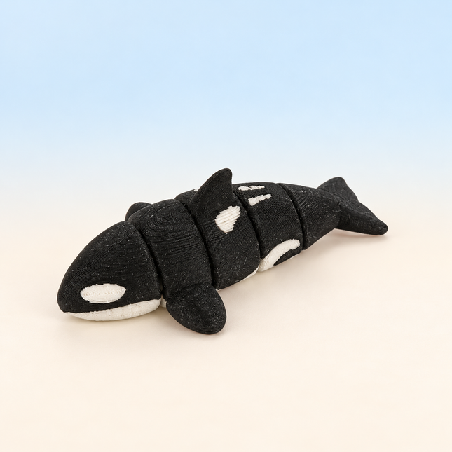 Micro Orca 3D-printed miniature featuring a black and white body, tall dorsal fin, and broad tail, on a light surface with a pale blue background.