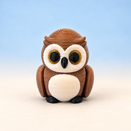 Micro Owl 3D-printed miniature with a brown body, cream belly, and large round eyes, on a light surface against a pale blue background.