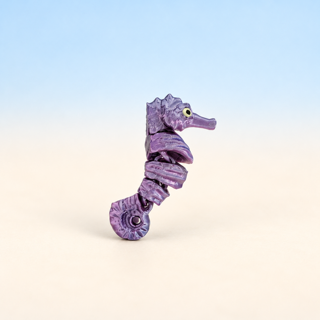 Micro Seahorse 3D-printed miniature featuring a purple body, ridged back, and curled tail, on a light surface with a pale blue background.