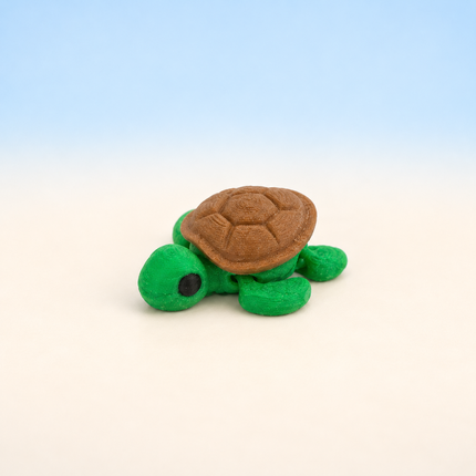 Micro Turtle 3D-printed miniature featuring a green body and a brown patterned shell, on a light surface with a pale blue background.
