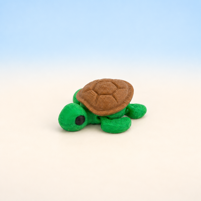 Micro Turtle 3D-printed miniature featuring a green body and a brown patterned shell, on a light surface with a pale blue background.